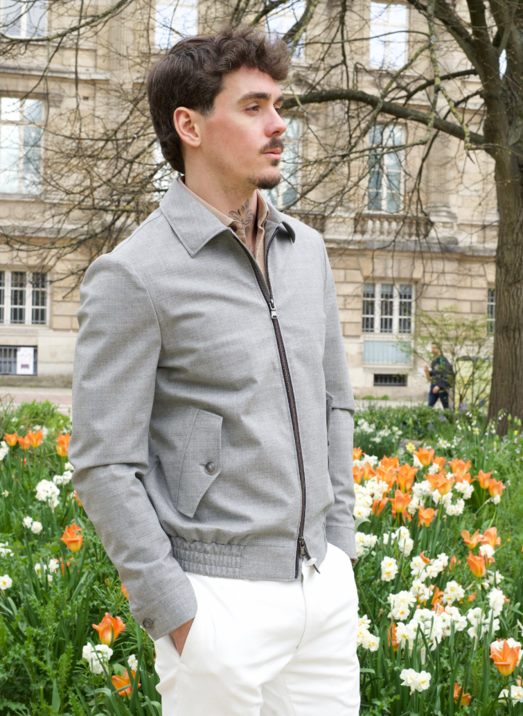Homme portant un blouson gris clair sur mesure avec fermeture zippée et pantalon blanc.