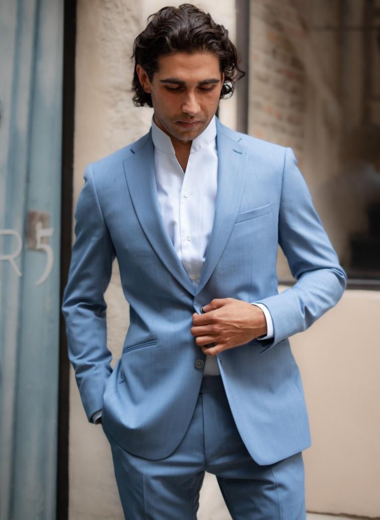 Homme portant un costume bleu ciel sur mesure avec chemise claire à col officier.